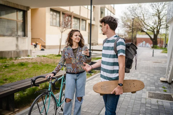 2人の若い大人のカップルの男性と女性のボーイフレンドとガールフレンドや学生の友人が自転車やスケートボード現代的なライフスタイルのコンセプトコピーペースで建物や大学で一日を歩く — ストック写真