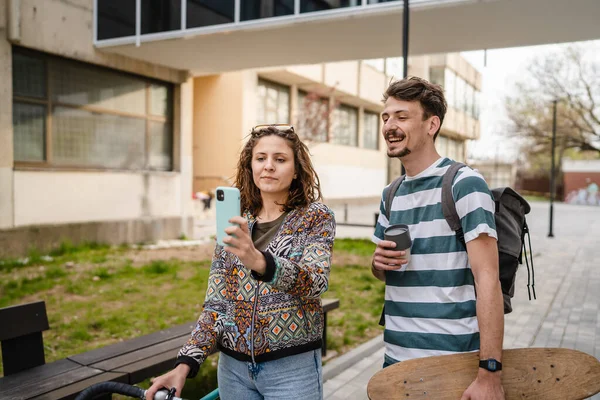 Two people young adult couple man and woman boyfriend girlfriend or students friends stand with mobile phone taking selfie photos or have video call on internet modern lifestyle concept copy pace