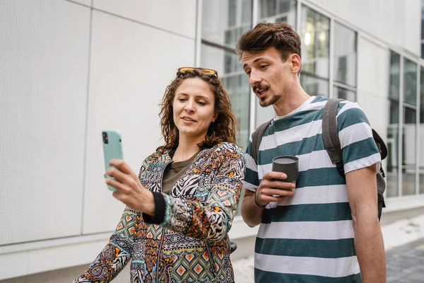 Two people young adult couple man and woman boyfriend girlfriend or students friends stand with mobile phone taking selfie photos or have video call on internet modern lifestyle concept copy pace