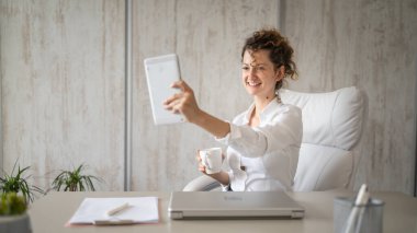 Genç bir iş kadını Kafkasyalı kadın dijital tablet kullanarak ofise geri dönüyor ve kahve girişimcisi modern iş konseptini içiyor.