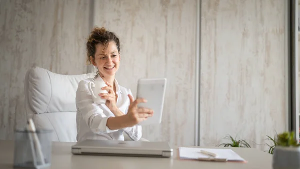 One young business woman caucasian female back to the office talking online using digital tablet while working and drinking coffee entrepreneur modern business concept