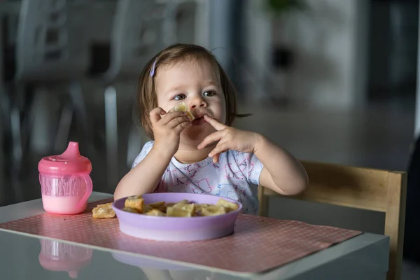 一人で家のテーブルに座っている一人の女の子の小さな白人の子供は 一日に一人で朝食やランチの食事のペストリーを食べます開発コンセプトコピースペースを成長現実の人々 — ストック写真
