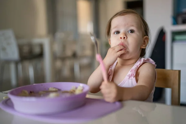 1人の子供小さな白人の幼児女性の赤ちゃんは 部屋の自宅で一人でテーブルで食べるスプーンを保持します — ストック写真