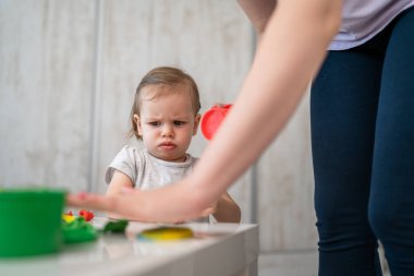 Annesi çocukluk konseptiyle uğraşırken ya da oyuncaklarını toplarken, ya da götürürken, evdeki masada mutsuz ya da kızgın oturan küçük, beyaz bir kız çocuğu.