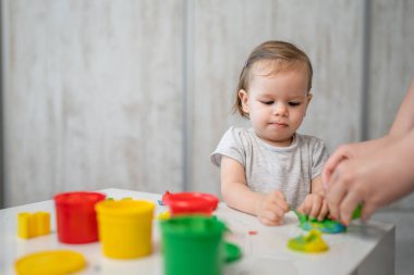 One girl small caucasian toddler child playing with colorful plasticine on the table at home alone childhood and growing up development concept copy space