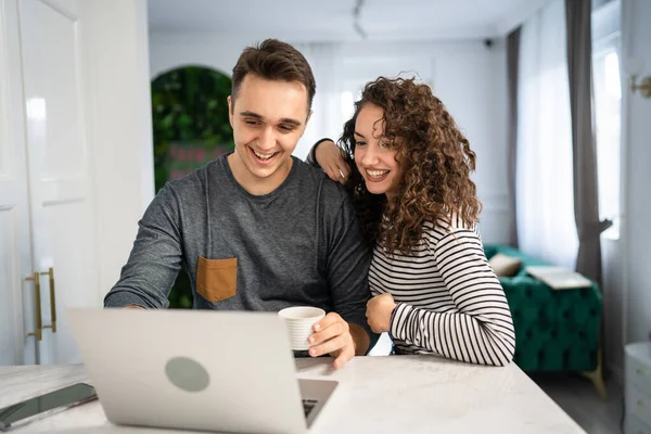 Two people young adult couple man and woman husband and wife or boyfriend and girlfriend in the kitchen with laptop computer checking online content shopping online or have video call morning routine