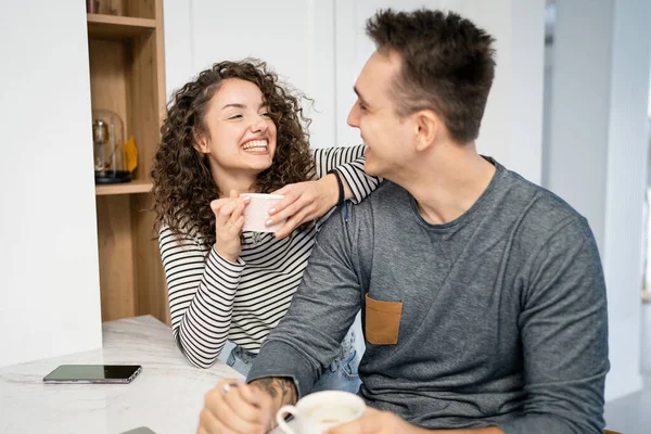 Two people young adult couple man and woman husband and wife or boyfriend and girlfriend in the kitchen with laptop computer checking online content shopping online or have video call morning routine