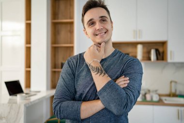 Genç, yetişkin, beyaz bir adamın portresi. Mutfakta gün boyu mutlu bir gülümseme. Kendine güveni tam.