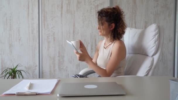 一位年轻的女商人回到办公室 一边工作一边喝着咖啡 一边用数码平板电脑在网上聊天 — 图库视频影像