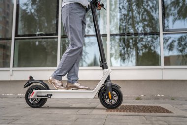 Bilinmeyen bir kadının ayakları kenarda duruyor ya da şehirde ya da kasabada, çevre dostu modern bir taşımacılıkta, kaldırımda elektrikli scooter kullanıyor.