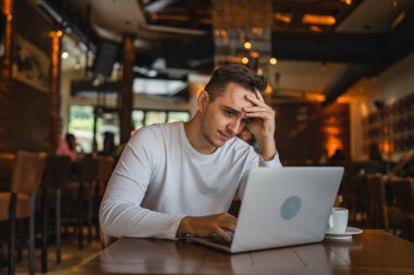 Kafe 'de dizüstü bilgisayarı olan genç, beyaz bir erkek bilgisayarda çalışıyor. Uzaktan kumandayla sorun çözüyor. Kriz raporları, durgunluk.