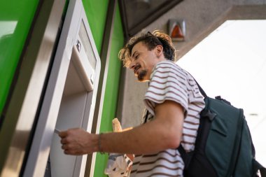 Bir adam genç yetişkin modern milenyum turisti ATM makinesiyle para çekmek için şehir yaşamını modern yaşam konseptini kullanıyor.