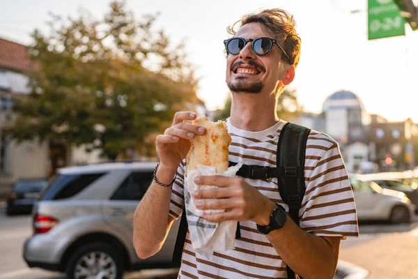 晴れた日の散歩で街の一人の若い大人の現代的な白人男性とサンドイッチを食べるファーストフードのコンセプト都市生活コピースペース観光客が路上で食べる本当の人幸せな笑顔 — ストック写真