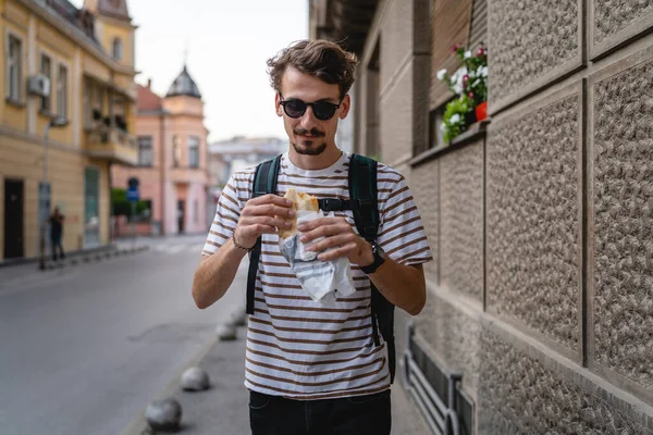 晴れた日の散歩で街の一人の若い大人の現代的な白人男性とサンドイッチを食べるファーストフードのコンセプト都市生活コピースペース観光客が路上で食べる実際の人 — ストック写真