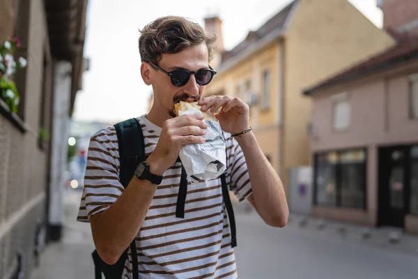 晴れた日の散歩で街の一人の若い大人の現代的な白人男性とサンドイッチを食べるファーストフードのコンセプト都市生活コピースペース観光客が路上で食べる実際の人 — ストック写真