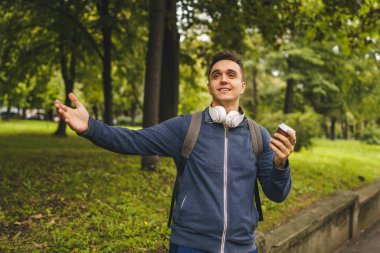 Genç, beyaz bir adam, sonbaharda ya da ilkbaharda elinde bir fincan kahveyle şehirde ya da parkın yakınında yürüyor. Mutlu bir erkek turist, tek başına duruyor.