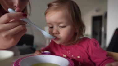 Küçük beyaz bir kız çocuğu, küçük bir kız çocuğu, küçük bir kız çocuğu, masada oturmuş, çocukluk kavramını beslerken, evde yemek yiyor. 