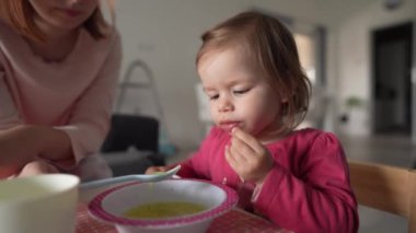 Küçük beyaz bir kız çocuğu, küçük bir kız çocuğu, küçük bir kız çocuğu, masada oturmuş, çocukluk kavramını beslerken, evde yemek yiyor. 