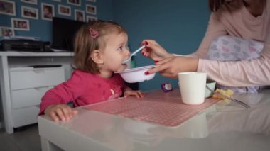 Küçük beyaz bir kız çocuğu, küçük bir kız çocuğu, küçük bir kız çocuğu, masada oturmuş, çocukluk kavramını beslerken, evde yemek yiyor. 