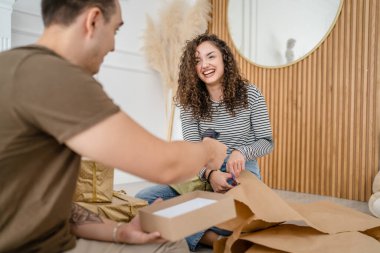 Birkaç erkek ve kadın tatil için hediyeler hazırlıyorlar. Beyaz erkek ve kadın arkadaşlara hediye paketliyor. Paket kağıttan gülücük kutusu kullanıyorlar.