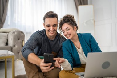 Erkek ve kadın mesajları okuyor ya da cep telefonunda internette geziniyor. Evde yerde otururken görüntülü konuşma yapıyor. Gerçek insanlar mutlu aile kavramı kopyalama alanı.