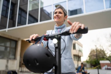 Bir kadın olgun, yaşlı, beyaz, açık havada elektrikli scooterlı bir kadın. Gündüz kendine güvenen bir iş kadını modern alternatif ulaşım yöntemini kullanıyor. Gerçek insanlar uzayı kopyalıyor.