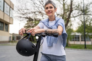 Bir kadın olgun, yaşlı, beyaz, açık havada elektrikli scooterlı bir kadın. Gündüz kendine güvenen bir iş kadını modern alternatif ulaşım yöntemini kullanıyor. Gerçek insanlar uzayı kopyalıyor.