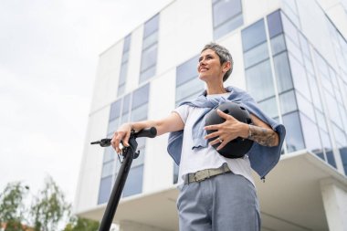Bir kadın olgun, yaşlı, beyaz, açık havada elektrikli scooterlı bir kadın. Gündüz kendine güvenen bir iş kadını modern alternatif ulaşım yöntemini kullanıyor. Gerçek insanlar uzayı kopyalıyor.