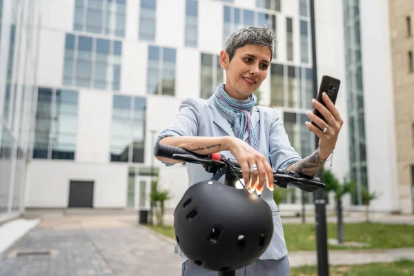1人の女性成熟したシニア白人女性立って屋外使用の携帯電話のための自撮り写真やビデオ通話電動キックスクーターによる日の自信を持って現代的な代替モードの輸送コピースペースミリ秒 — ストック写真