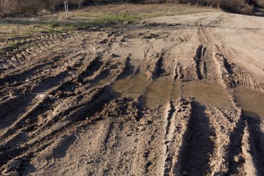 Güneşli bir bahar gününde yağmurdan sonra çamurlu su birikintileriyle dağlarda toprak yol.
