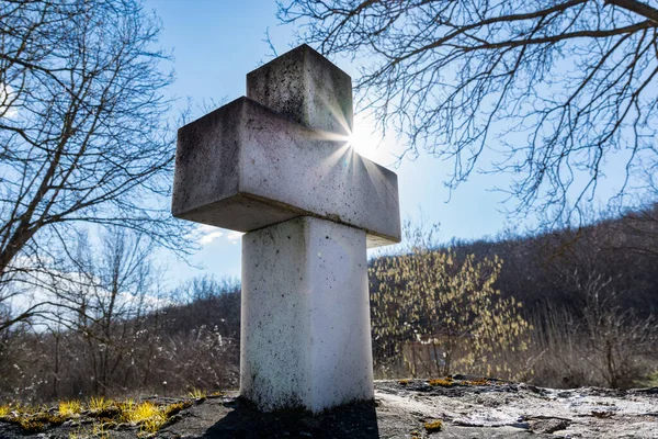 Beyaz mermer dini haç, arka planda güneş ışığı ve güneş var. Doğada bir bahar günü gün batımında. Yaklaş, seçici odaklanma
