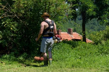 Çiftçi, eski evin arkasındaki güneşli bir yaz gününde arka bahçede bir el çim biçme makinesiyle uzun çimleri biçti. Bahçe konsepti