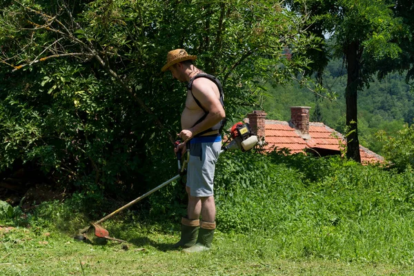 在一个阳光明媚的夏日里 那个戴着草帽的农民在后院用割草机割草 园艺概念 — 图库照片
