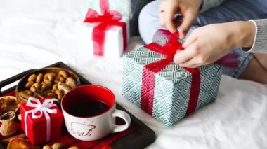 Hediyeler paketleniyor. Kadın hediye kutusunu kırmızı kurdeleyle bağlıyor, yakın çekim. Kapalı bir Noel etkinliği