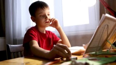 Evdeki masada ödev yapan konsantre olmuş beyaz bir çocuğun portresi. Düşünceli okul çocuğu. Eğitim, öğrenim, öğrenim