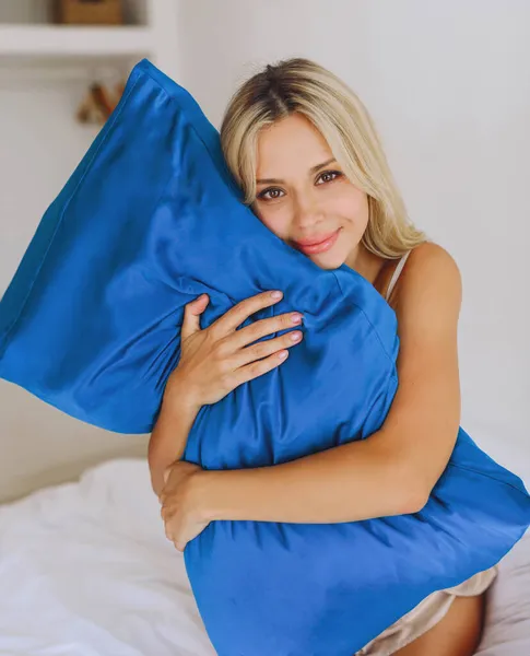床上的欧洲金发女郎抱着一个有丝绸枕套的枕头 — 图库照片