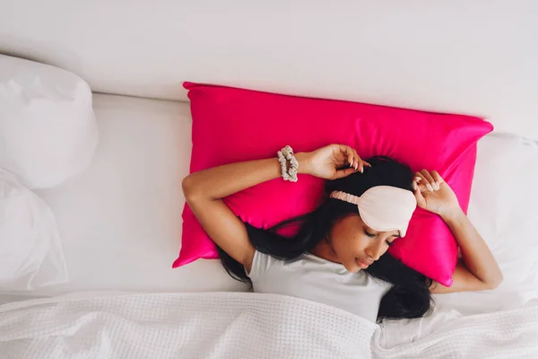 美しいインドネシアの少女は シルクの枕ケースと睡眠マスクを持つ明るいピンクの枕に横たわっています アブーからの眺め — ストック写真