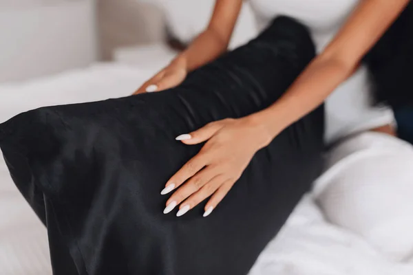 The girl\'s hands are stroking the pillow with a silk pillowcase. Focus on the pillowcas