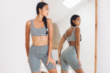 Tatlı Asyalı kız aynanın yanında spor giyim sergiliyor ve yansıyor.