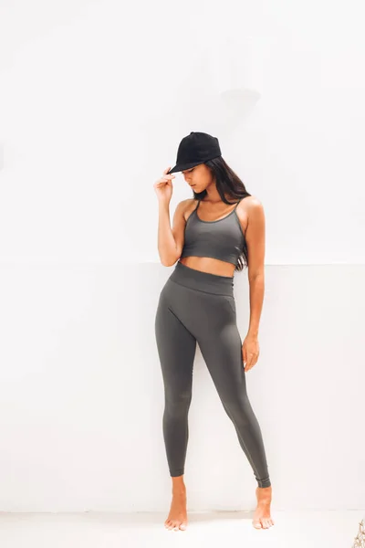 Fitnes spor modelinin Asyalı modeli beyaz duvarın üzerinde moda spor kıyafetleriyle poz veriyor.