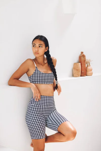 Fitnes spor modelinin Asyalı modeli beyaz duvarın üzerinde moda spor kıyafetleriyle poz veriyor.