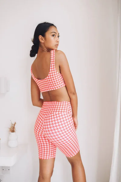Fitnes spor modelinin Asyalı modeli beyaz duvarın üzerinde moda spor kıyafetleriyle poz veriyor.