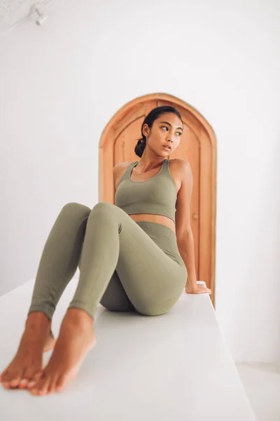 Fitnes spor modelinin Asyalı modeli beyaz duvarın üzerinde moda spor kıyafetleriyle poz veriyor.