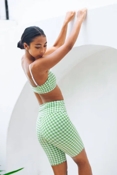 Fitnes spor modelinin Asyalı modeli beyaz duvarın üzerinde moda spor kıyafetleriyle poz veriyor.