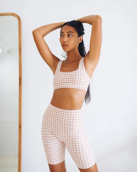 Fitnes spor modelinin Asyalı modeli beyaz duvarın üzerinde moda spor kıyafetleriyle poz veriyor.