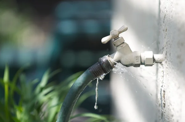 A water spigot with a green hose springs a leak — Stock Photo, Image