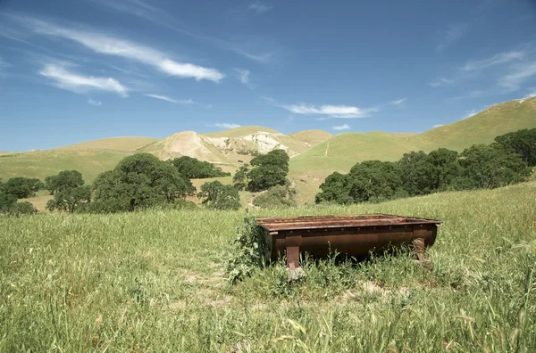 Rusty old cattle water trough near hills — Stock Photo, Image