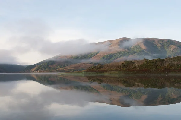 Heuvels weerspiegeld in oppervlak van lake mistige ochtend — Stockfoto