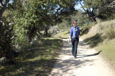 Woman hikes up dirt fireroad, away from camera, empty space left