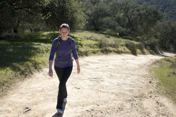 Woman in pants hikes up dirt fireroad, empty space right — Stock Photo, Image